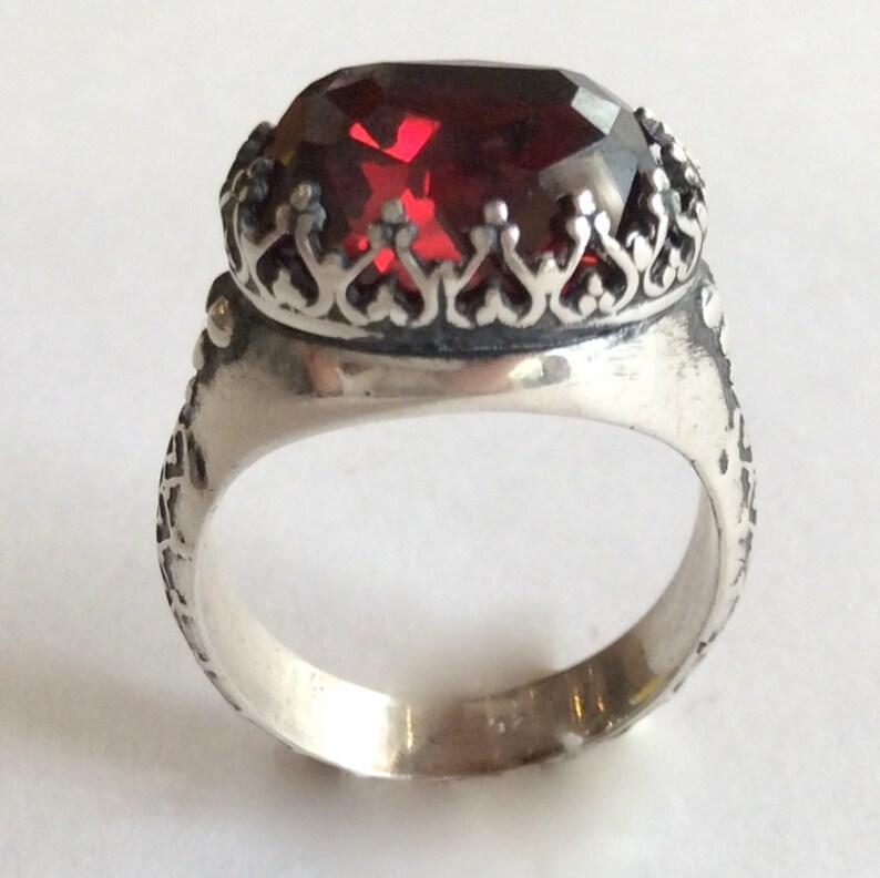 Puede incluir: Un anillo de plata con un dise&ntilde;o ornamentado y una gran piedra preciosa roja en el centro.