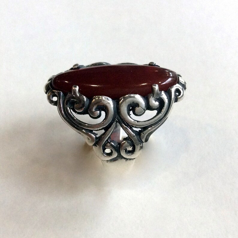 May include: A silver ring with a red oval gemstone set in a filigree design.
