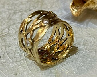 May include: A gold ring with a delicate, intricate design featuring a woven pattern and three small, clear gemstones.