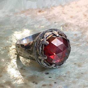 Puede incluir: Un anillo de plata con una gran piedra preciosa roja facetada engastada en un engaste de plata detallado y ornamentado.