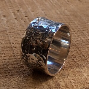 May include: A wide silver band ring with a textured, hammered finish. The ring has a smooth, polished interior.