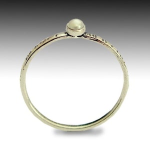 Puede incluir: Un anillo de plata sencillo con una pequeña perla blanca engastada en el centro. La banda del anillo tiene un diseño texturizado.