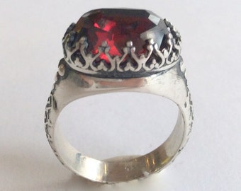 Pode incluir: Um anel de prata com um design ornamentado e uma grande pedra preciosa vermelha no centro.