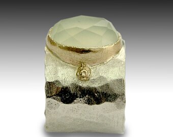 May include: A silver ring with a hammered texture and a gold band set with a light green gemstone.