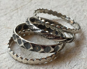 May include: Four silver stacking rings with different textures. The top ring has a beaded design, the second ring has a floral design, the third ring has a hammered texture, and the bottom ring has a beaded design.