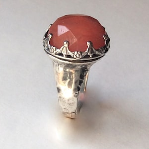 Puede incluir: Un anillo de plata con una gran piedra preciosa rosa facetada engastada en un engaste decorativo de corona.
