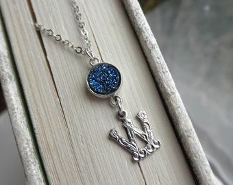 Könnte beinhalten: Eine silberne Halskette mit einem blauen Glitzer-Anhänger und einem silbernen Anhänger in Form des Buchstabens W.