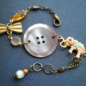 May include: A bracelet with a large, brown button, a pink and green elephant charm, a gold bow, and a small orange bead.