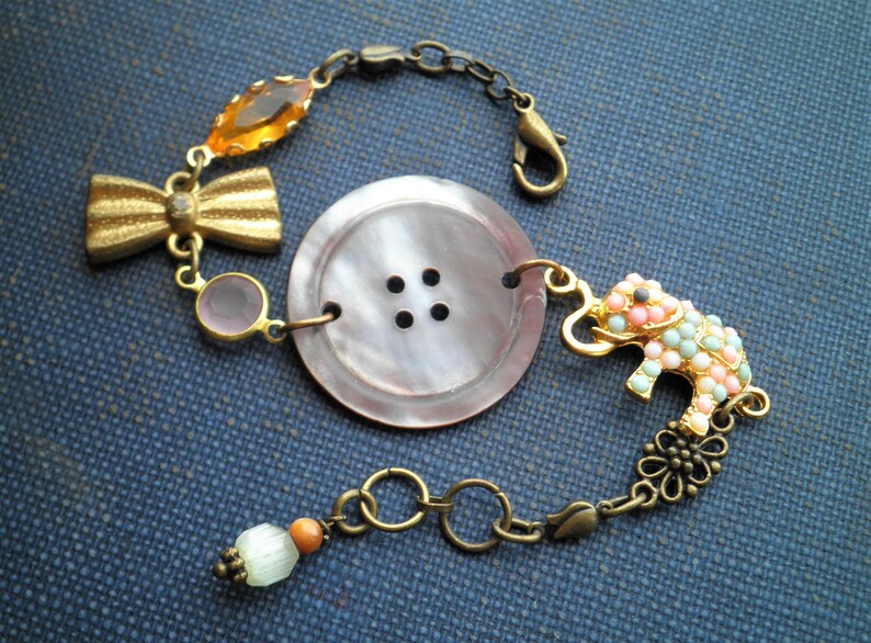 May include: A bracelet with a large, brown button, a pink and green elephant charm, a gold bow, and a small orange bead.