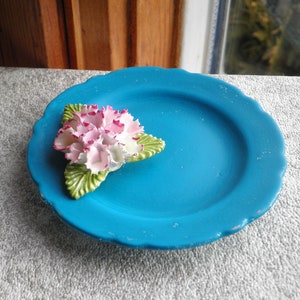 May include: A small, blue ceramic plate with a white and pink flower with green leaves.