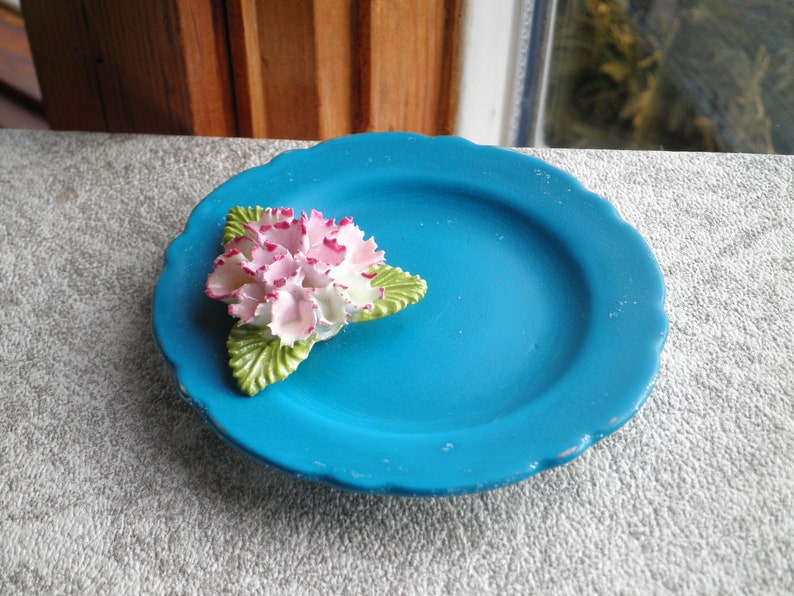 May include: A small, blue ceramic plate with a white and pink flower with green leaves.