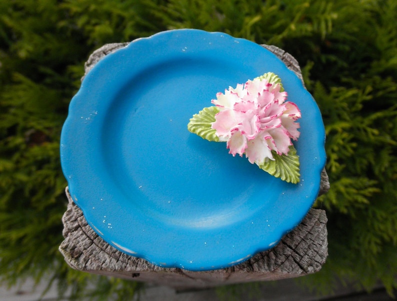 May include: A blue ceramic plate with a white and pink flower design. The plate has a scalloped edge and is sitting on a wooden surface.