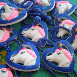 May include: A group of blue heart-shaped hair ties with a white unicorn head design. Each unicorn has a pink mane and horn with a rainbow stripe.