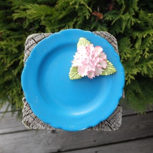 May include: A small blue ceramic plate with a white flower on top. The plate is sitting on a wooden surface.