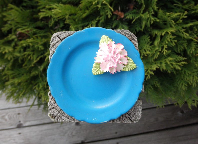 May include: A small blue ceramic plate with a white flower on top. The plate is sitting on a wooden surface.