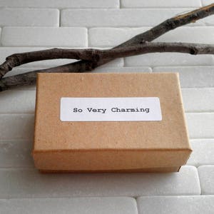 May include: A brown cardboard box with a white label that says "So Very Charming".