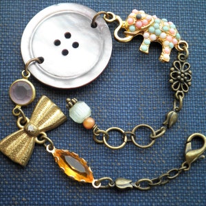 May include: A charm bracelet with a large, brown button, a gold bow, a pastel pink and blue elephant charm, and a variety of other beads and charms.