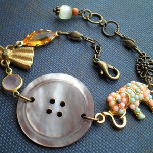 May include: A bracelet with a large, pearly button, a pink crystal, a gold bow, a beaded elephant charm, and a chain with a clasp.