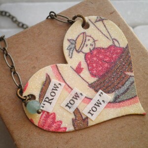 May include: A heart-shaped pendant necklace with a glittery, colorful design. The pendant features a vintage illustration of a child wearing a red and white dress. The pendant also has the words "Row, row, row" written on it.