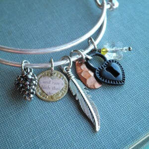 May include: A silver charm bracelet with multiple charms, including a small pine cone, a heart-shaped charm with the text "and rare a which they", a copper-colored charm, a feather charm, and a black heart-shaped lock charm.