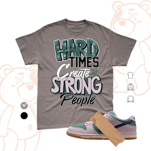 May include: A gray t-shirt with the text "HARD TIMES create STRONG People" in a stylized font. The shirt is paired with a pair of purple and green sneakers with a brown sole. The brand name "NASTY JAMZ" is printed on the shirt.