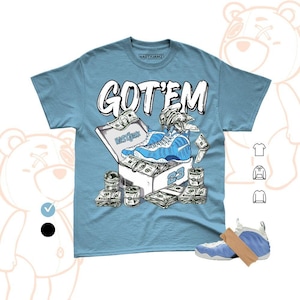 May include: Light blue t-shirt with the text "GOT'EM" in white. The graphic features a blue and white sneaker in a shoebox with money and the number 23. A pair of blue and white sneakers are also in the image.