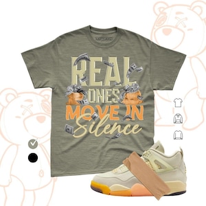 May include: An olive green short-sleeve t-shirt featuring the text "REAL ONES MOVE IN SILENCE" in cream and orange, accompanied by illustrations of two brown money bags and flying dollar bills, paired with a cream and orange athletic sneaker.