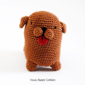 May include: A brown crocheted dog toy with a red tongue sticking out. The dog has black eyes and a black nose.