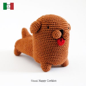 May include: A brown crocheted dog toy with a red tongue sticking out. The toy has black eyes and a brown nose.
