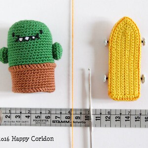 May include: A green crocheted cactus with a brown pot and a smiling face, and a yellow crocheted skateboard with black wheels.