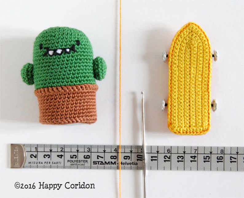 May include: A green crocheted cactus with a brown pot and a smiling face, and a yellow crocheted skateboard with black wheels.