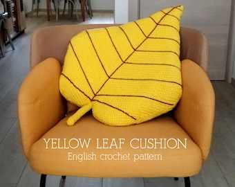May include: A yellow crocheted leaf cushion with brown stitching. The cushion is sitting on a brown armchair. The text "YELLOW LEAF CUSHION" and "English crochet pattern" is printed below the cushion. The text "©2024 Coridon" is printed below the text.