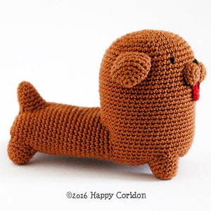 May include: A brown crocheted dachshund plush toy with a red tongue sticking out. The toy has black eyes and a stitched nose.