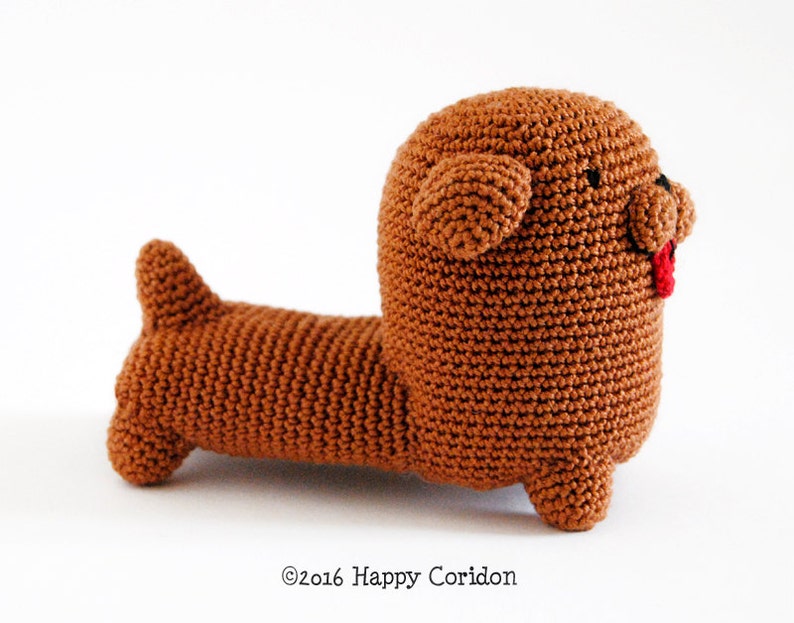 May include: A brown crocheted dachshund plush toy with a red tongue sticking out. The toy has black eyes and a stitched nose.