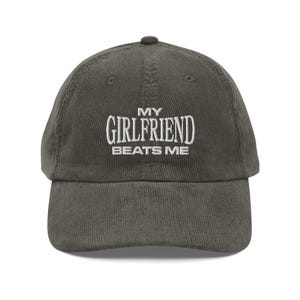 May include: A dark green corduroy baseball cap with white embroidered text that reads "My Girlfriend Beats Me."