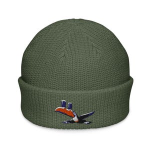 May include: A green knitted beanie with a toucan design embroidered on the front. The toucan is holding two glasses in its beak.