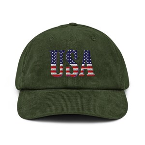 May include: A green corduroy baseball cap with the word "USA" embroidered on the front. The letters are designed with the American flag's stars and stripes. The cap has a curved brim and an adjustable strap.