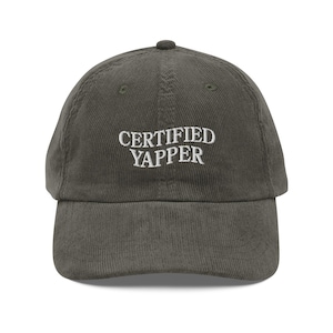 May include: A dark green corduroy baseball cap with white embroidered text that reads "CERTIFIED YAPPER".