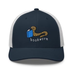 Op de afbeelding: Marineblauwe en witte truckerpet met een geborduurde cartoon boekenwurm die een blauw boek vasthoudt. Het woord "bookworm" is eronder geborduurd. De pet heeft een gebogen klep en een mesh achterkant.