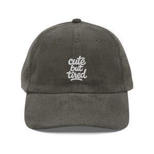 Könnte beinhalten: Olivgrüne Cord-Baseballkappe mit gebogenem Schirm. Auf der Kappe ist der Text "cute but tired" in weißer Schrift gestickt. Die Kappe hat ein klassisches Sechs-Panel-Design und einen verstellbaren Riemen.