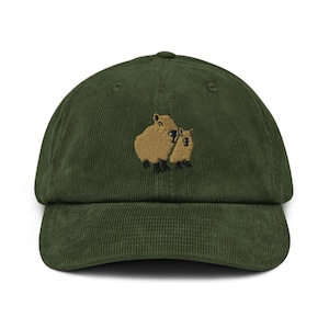 May include: A dark green corduroy baseball cap featuring an embroidered design of two capybaras. The capybaras are in shades of brown and black. The cap has a curved brim and an adjustable strap at the back.