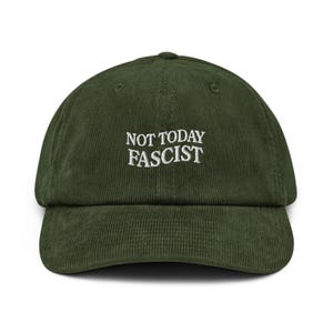 以下が含まれることがあります： 白い文字で「NOT TODAY FASCIST」と刺繍された、濃い緑色のコーデュロイベースボールキャップ。 キャップはカーブしたつばと丸いクラウンが特徴です。