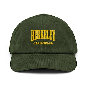 Może przedstawiać: Ciemnozielona czapka z daszkiem z sztruksu z żółtym napisem "BERKELEY" i napisem "CALIFORNIA" poniżej. Czapka ma zakrzywiony daszek i zapięcie na pasek z tkaniny.