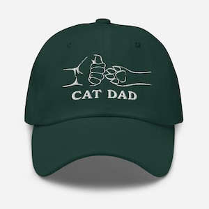 May include: A dark green baseball cap with white embroidery of a cat paw and human hand shaking, with the text "CAT DAD" below.