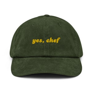 May include: A green corduroy baseball cap with the text "yes, chef" embroidered in yellow.