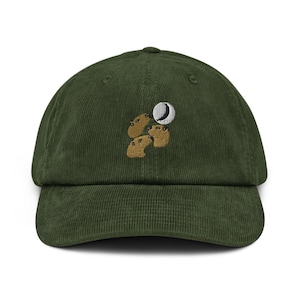 Può includere: Cappellino da baseball in velluto a coste verde scuro con un design ricamato. Il design presenta tre capibara marroni e una luna crescente. Il cappellino ha una visiera curva e un cinturino regolabile sul retro.