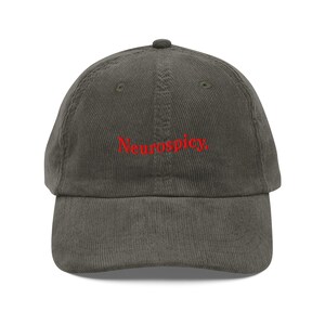 Könnte beinhalten: Eine olivgrüne Cord-Baseballkappe mit dem roten Wort "Neurospicy" auf der Vorderseite. Die Kappe hat einen gebogenen Schirm und einen verstellbaren Riemen auf der Rückseite.