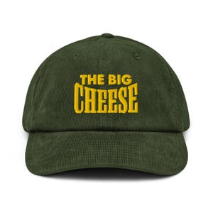 Pode incluir: Boné de beisebol de veludo cotelê verde com a inscrição "THE BIG CHEESE" bordada em amarelo. O boné tem uma aba curva e uma alça ajustável na parte de trás.