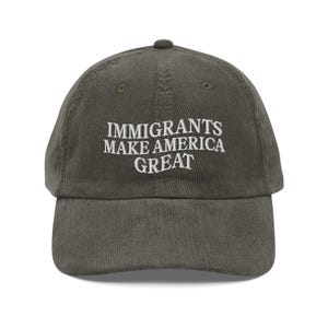 Könnte beinhalten: Eine dunkelgrüne Baseballkappe aus Cord mit dem in Weiß gestickten Schriftzug "Immigrants Make America Great" auf der Vorderseite.