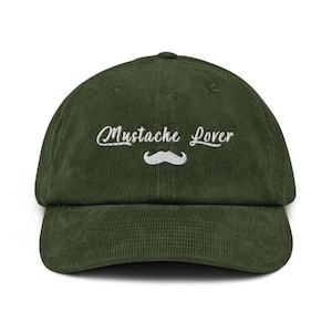 May include: A green corduroy baseball cap with the embroidered text "Mustache Lover" above a white mustache graphic. The cap has a curved brim and a structured crown, suitable for casual wear.